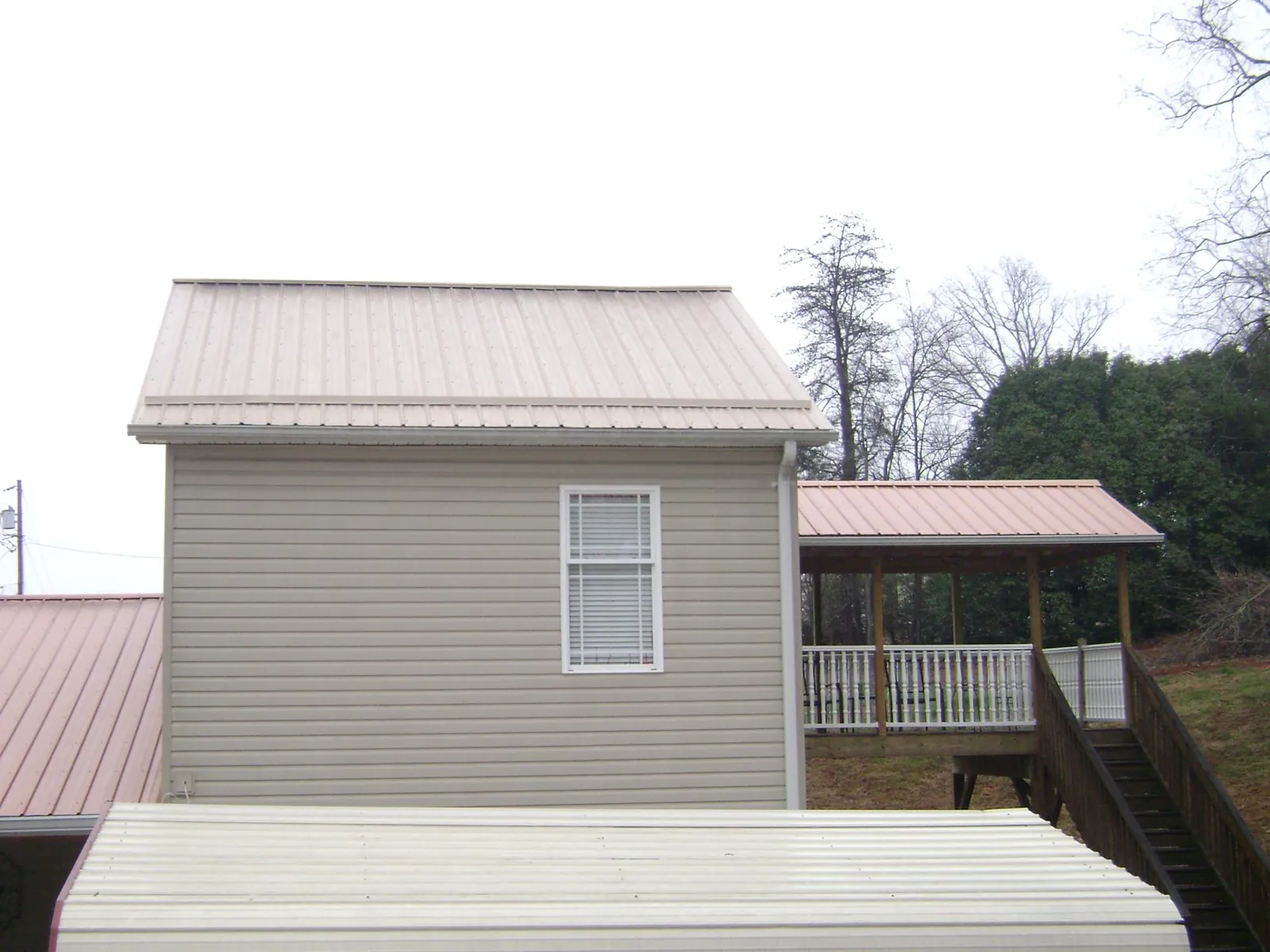 Tan metal roofs on a two story addition and attached porch, from a Roof Replacement job in Gardner